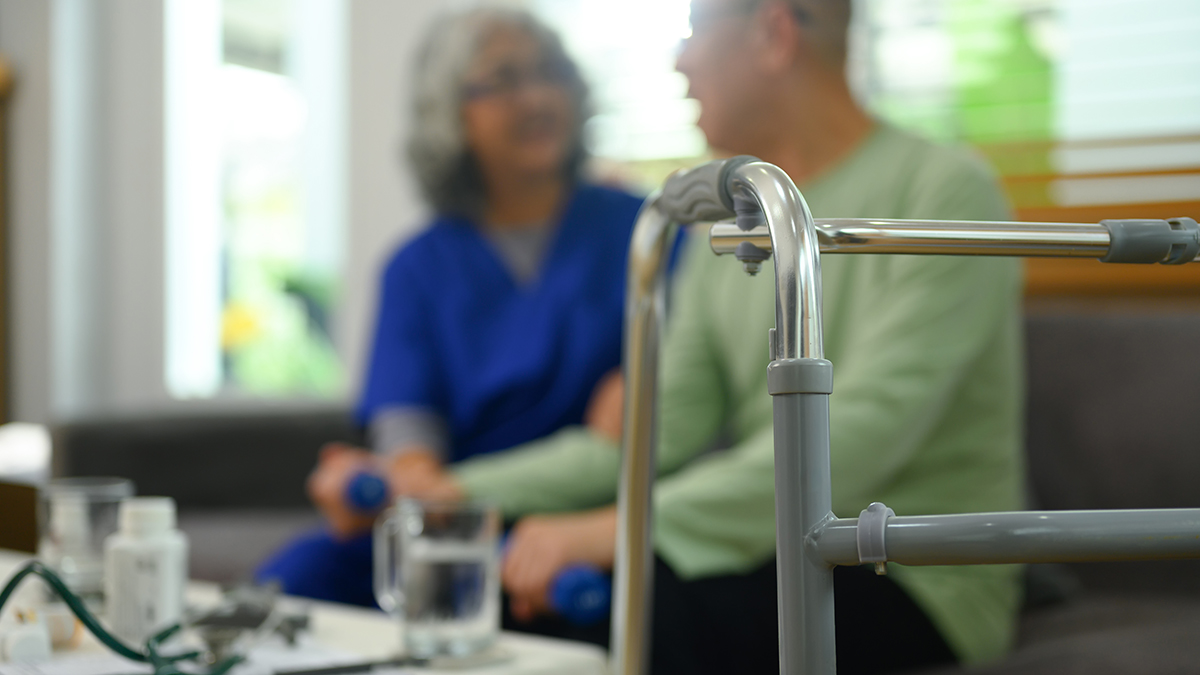 Select focus on metal walking frame against blurred doctor consulting elderly patient in a nursing home